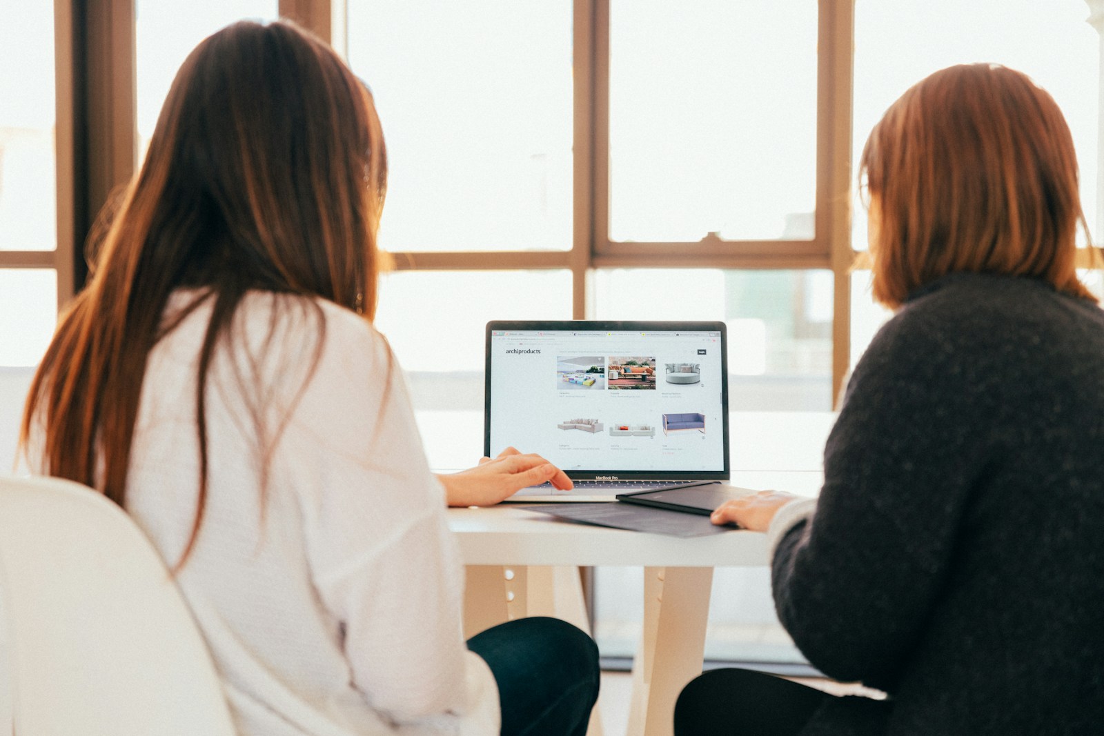 dwie kobiety rozmawiają patrząc na ekran laptopa