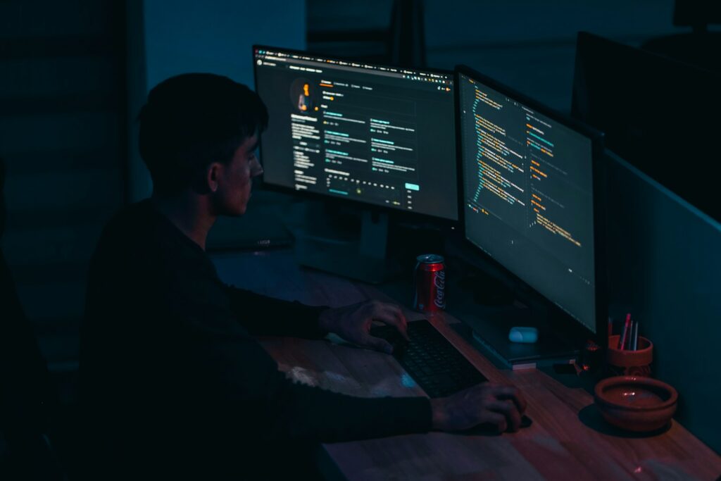 mężczyzna w czarnej bluzie programuje przy komputerze